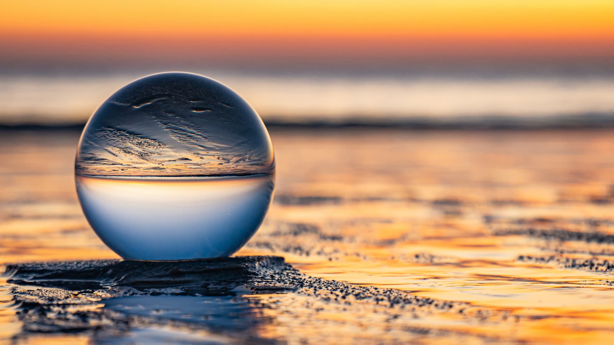 Kompetenz & Erfahrung bei maximaler Flexibilität Eine Glaskugel am Wasser, in der sich ein Sonnenuntergang spiegelt.